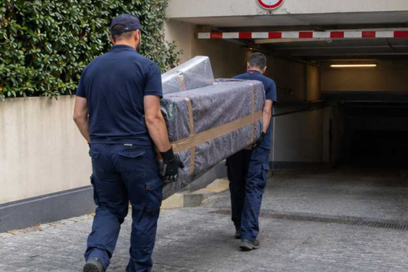 Deux déménageurs portent des meubles emballés sous couvertures, entrée de parking souterrain à hauteur limitée