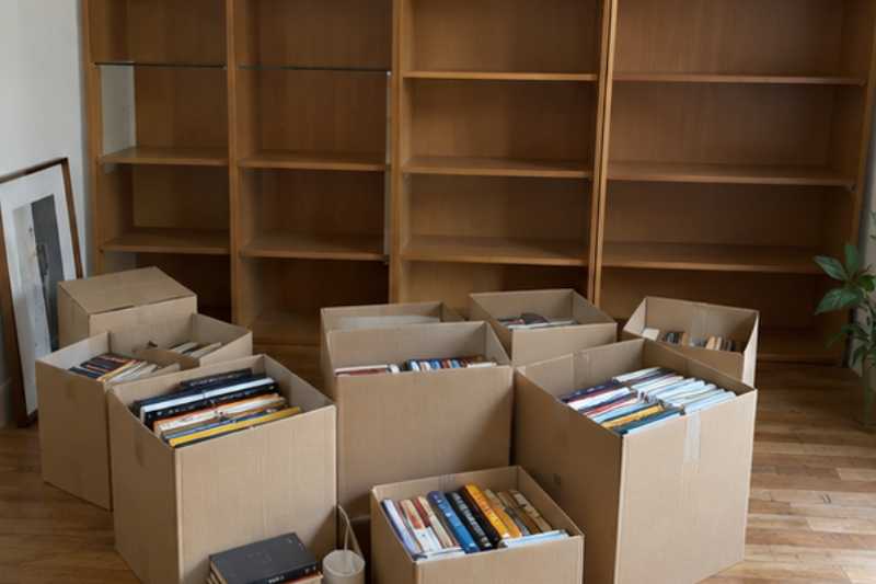 Bibliothèque vidée et livres rangés dans de petits cartons