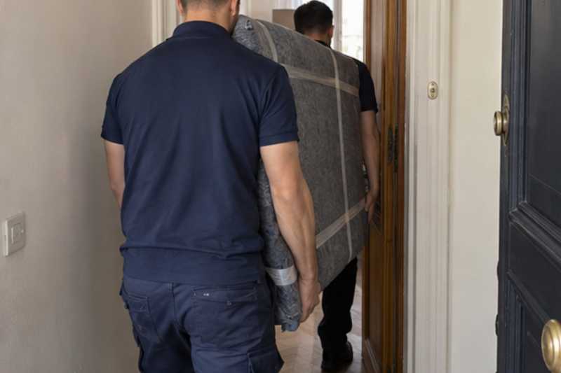 Deux déménageurs portent des meubles emballés sous couvertures, porte palière étroite d'appartement