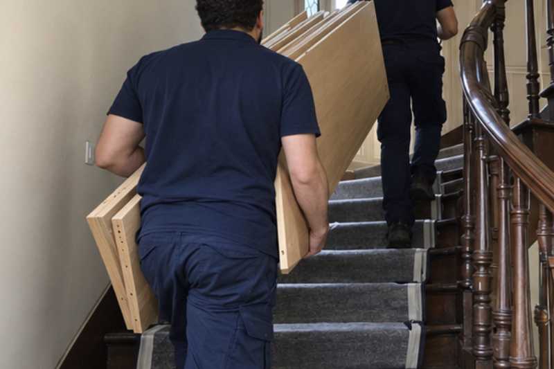 Déménageurs qui portent les éléments d'une grande bibliothèque démontée, escalier ancien en bois aux marches couvertes de protections