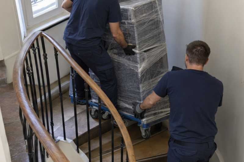 Déménageurs qui roulent du mobilier de bureau emballé sur des chariots, escalier tournant avec un palier étroit