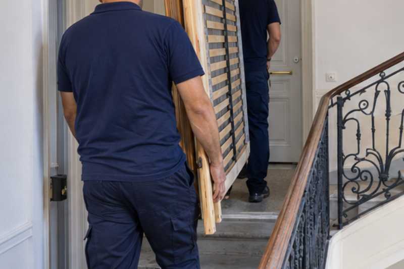 Déménageurs qui portent un sommier et les montants d'un lit démonté, dernier palier d'un escalier sans ascenseur