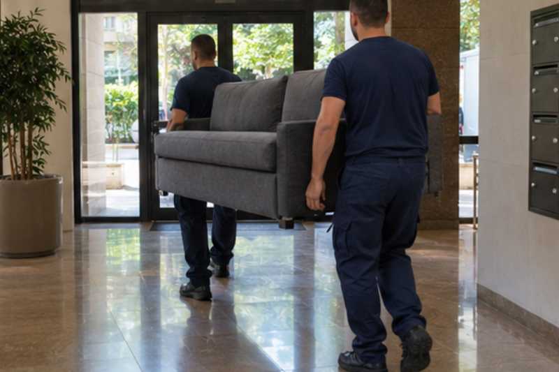 Deux déménageurs manœuvrent un canapé convertible lourd, hall d'immeuble résidentiel