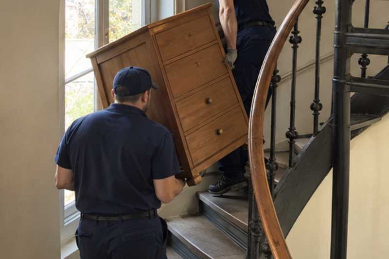 Déménageurs qui portent une commode dans un escalier en colimaçon