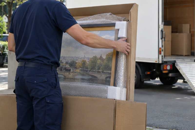 Déménageur qui emballe un tableau encadré dans un carton de protection